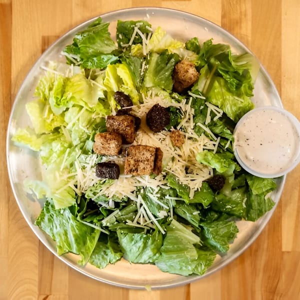 Caesar salad with romaine lettuce, croutons, shredded Parmesan cheese, and a side of dressing.