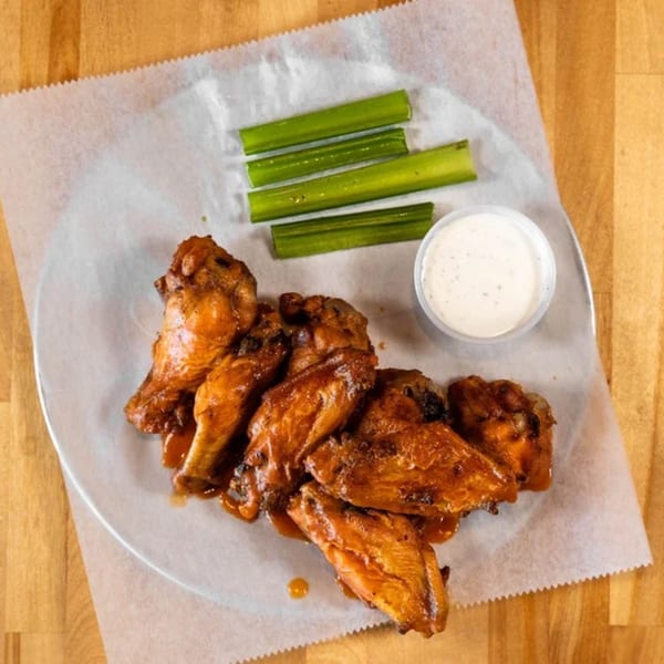 A plate of Five Bros Pizza's chicken wings with celery sticks and a side of ranch dressing.