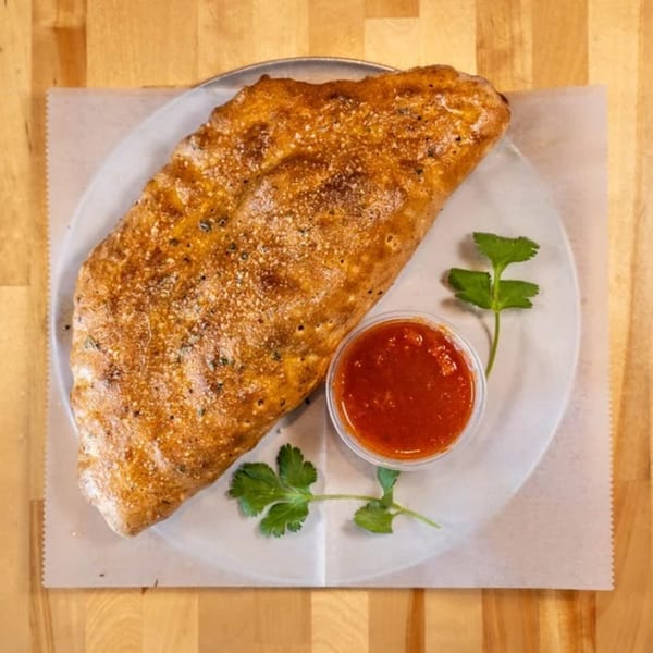 A golden-brown calzone from Five Bros Pizza, served with a side of red marinara sauce and parsley.